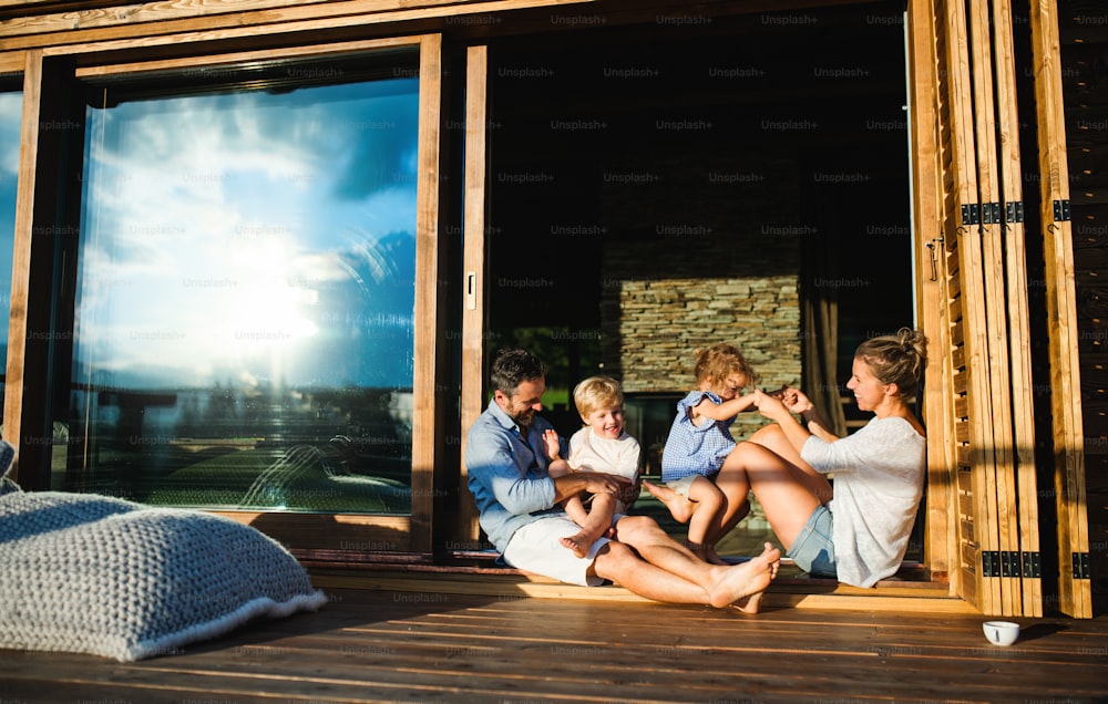 Happy family with small children sitting on patio of wooden cabin, holiday in nature concept.