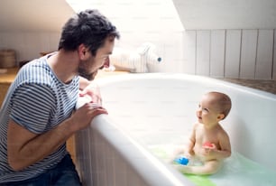 Vater wäscht ein Kleinkind in der Badewanne im Badezimmer zu Hause. Vaterschaftsurlaub.