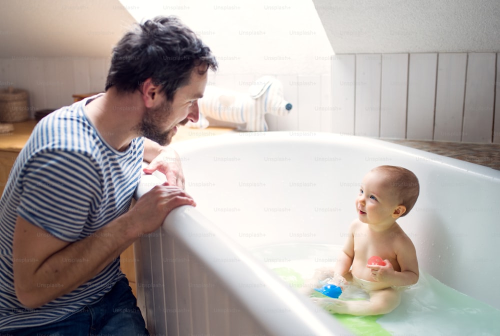 Padre che lava un bambino nella vasca da bagno nel bagno di casa. Congedo di paternità.