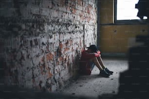 Ragazzo adolescente triste e deluso seduto su una sedia all'interno di un edificio abbandonato.