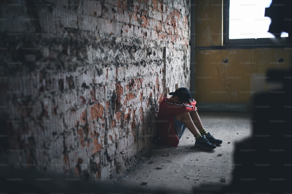 Sad and disappointed teenagers boy sitting on chair indoors in abandoned building.