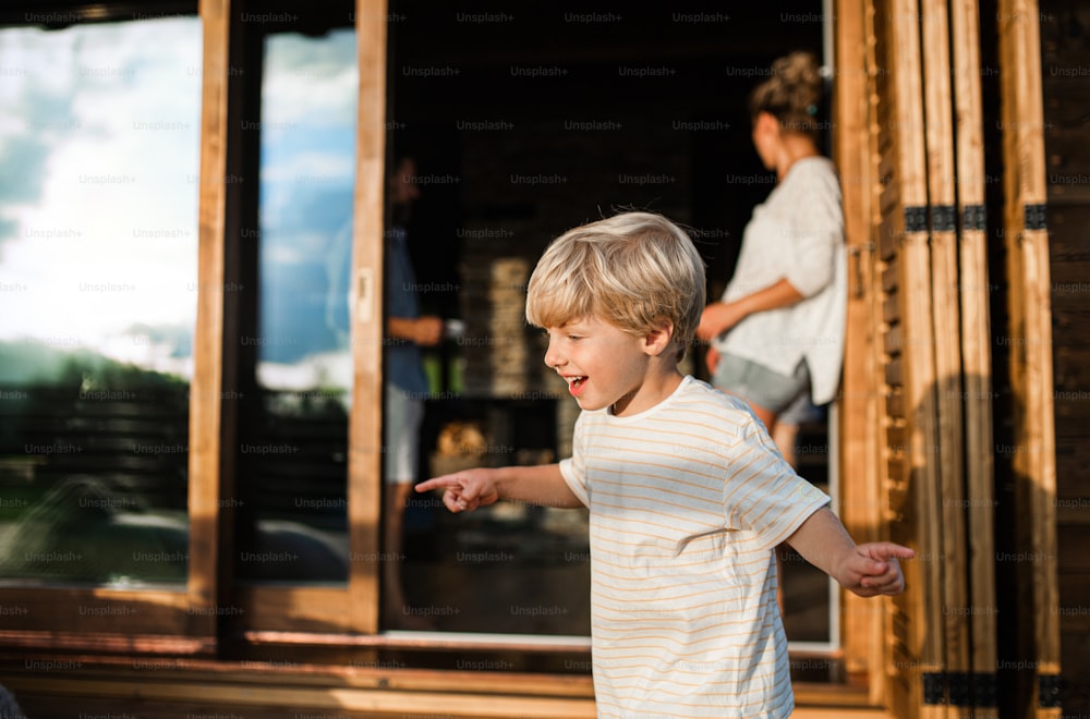 Fröhlicher kleiner Junge mit Eltern auf der Terrasse der Holzhütte, Urlaub in der Natur Konzept.