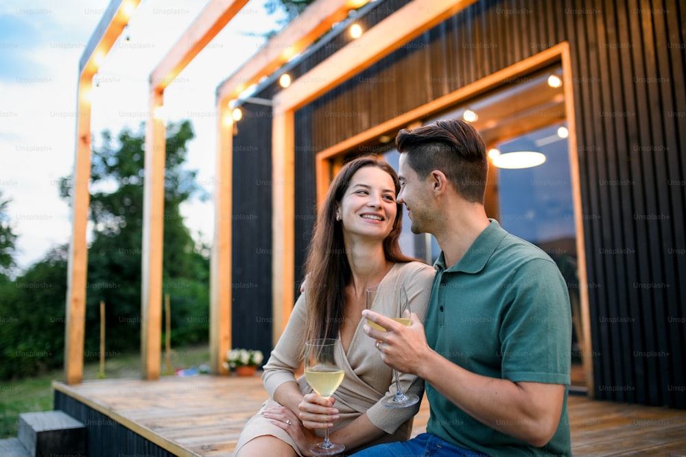 Giovane coppia con vino seduta all'aperto, fine settimana in casa container in campagna.