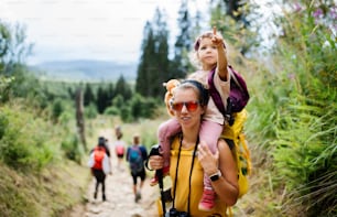 Front view of mother with small toddler daughter hiking outdoors in summer nature, looking at camera.