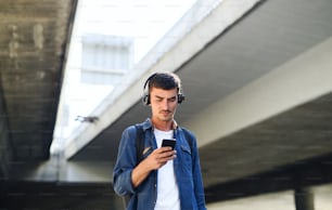 Vue en contre-plongée d’un jeune homme attrayant avec des écouteurs debout à l’extérieur dans la ville. Espace de copie.