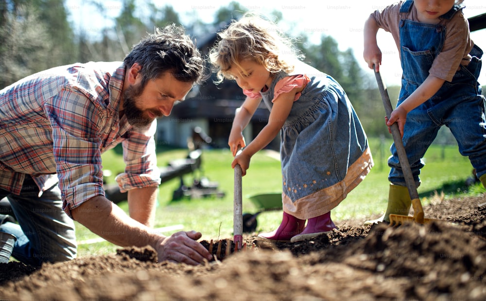 Père mûr avec de jeunes enfants travaillant à l’extérieur dans le jardin, concept de mode de vie durable.
