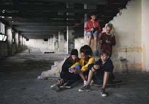 Vue de face d’un groupe d’adolescents assis à l’intérieur dans un bâtiment abandonné, à l’aide de smartphones.