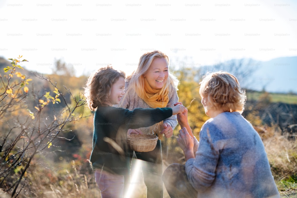秋の自然の中でローズヒップの実を集めている母と祖母を持つ幸せな小さな女の子。