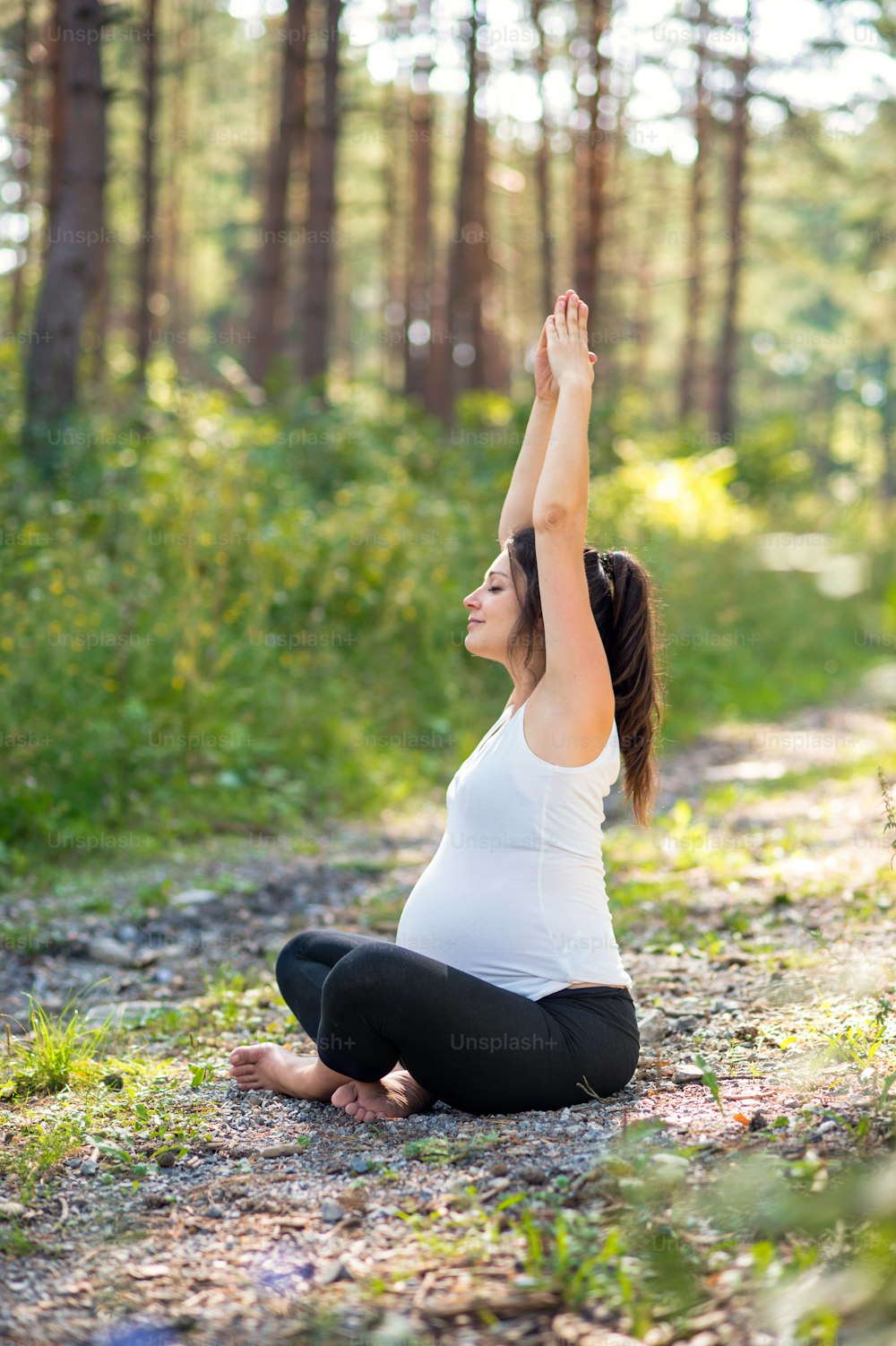 Side view portrait of happy pregnant woman outdoors in nature, doing yoga exercise.