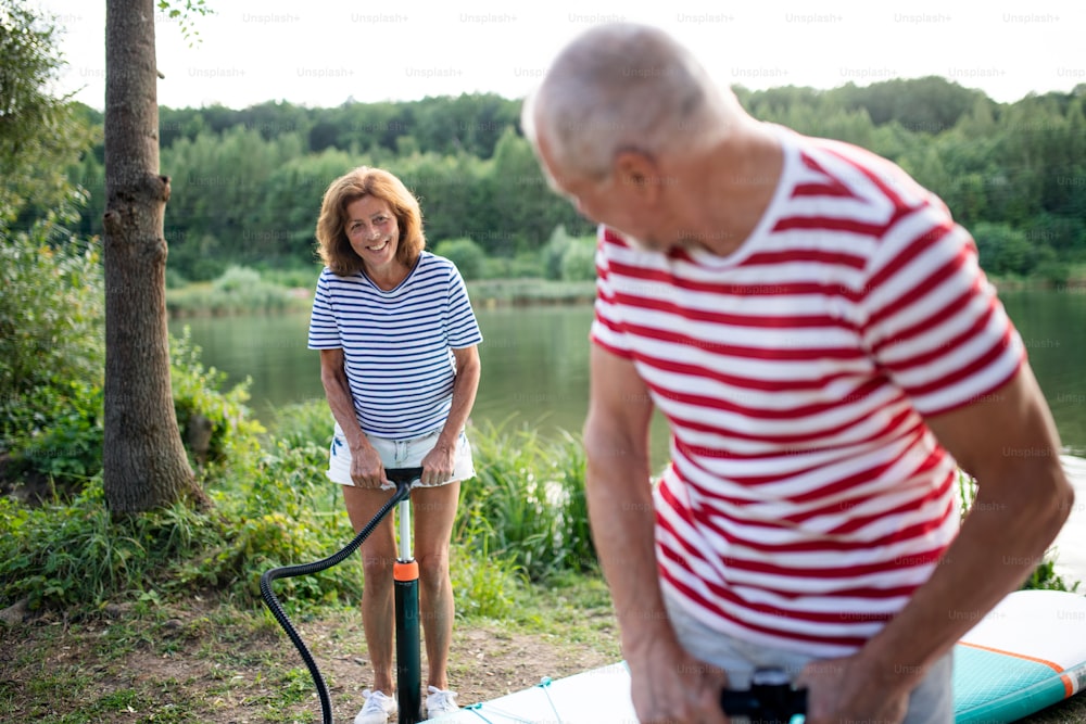 Active senior couple getting ready for paddleboarding by lake in summer.
