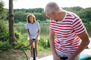 Active senior couple getting ready for paddleboarding by lake in summer.