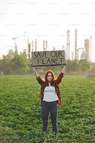 Retrato de una joven activista con un cartel de pie al aire libre junto a la refinería de petróleo, protestando.