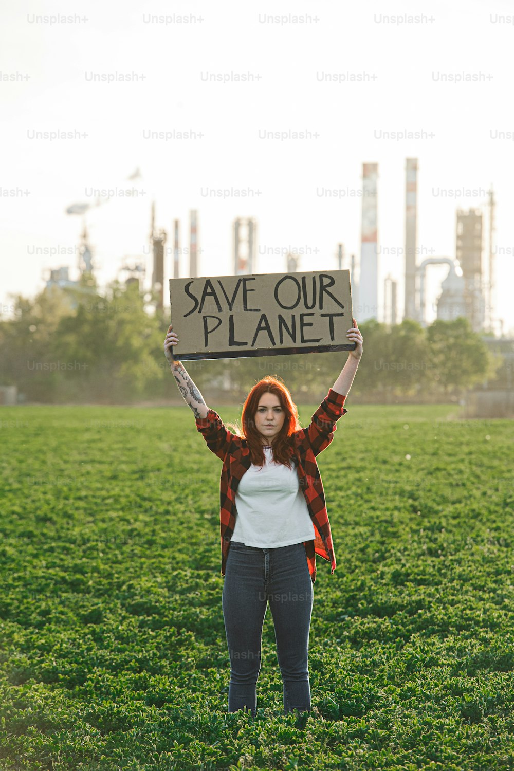 石油精製所のそばの屋外に立って抗議するプラカードを持った若い女性活動家の肖像画。