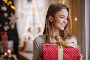Portrait de jeune femme heureuse à l’intérieur à la maison à Noël, tenant un cadeau.