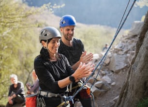 Un grupo de personas mayores con instructor que usa tiza antes de escalar rocas al aire libre en la naturaleza, estilo de vida activo.