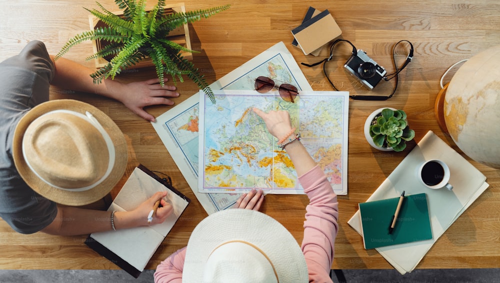 休暇旅行の休日、デスクトップ旅行のコンセプトを計画している地図を持つ認識できない若いカップルの上面図。
