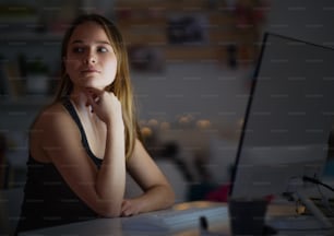 Young girl with computer sitting at desk at night, online dating concept. Copy space.