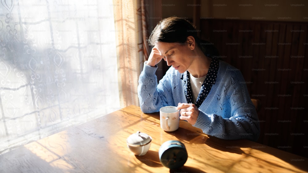 Porträt einer unglücklichen armen reifen Frau mit Kaffee drinnen zu Hause, Armutskonzept.