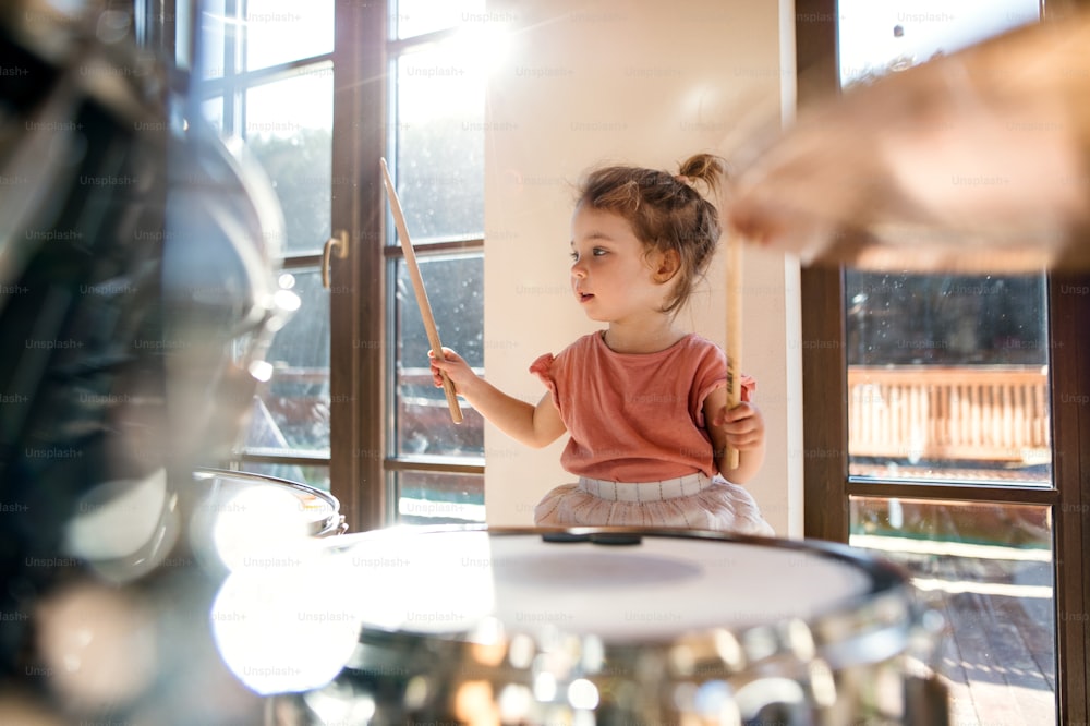집에서 실내에서 드럼을 연주하는 행복한 작은 소녀의 초상화.