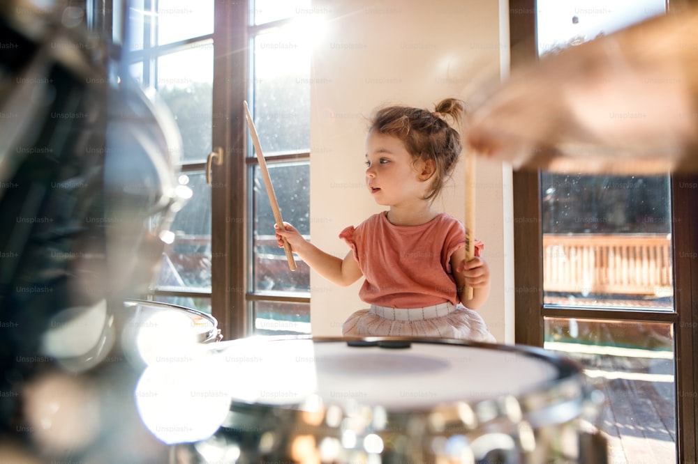 Portrait of happy small girl indoors at home, playing drums.