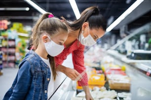 スーパーマーケットで食べ物を買うフェイスマスクをした母と小さな娘、コロナウイルスのコンセプト。