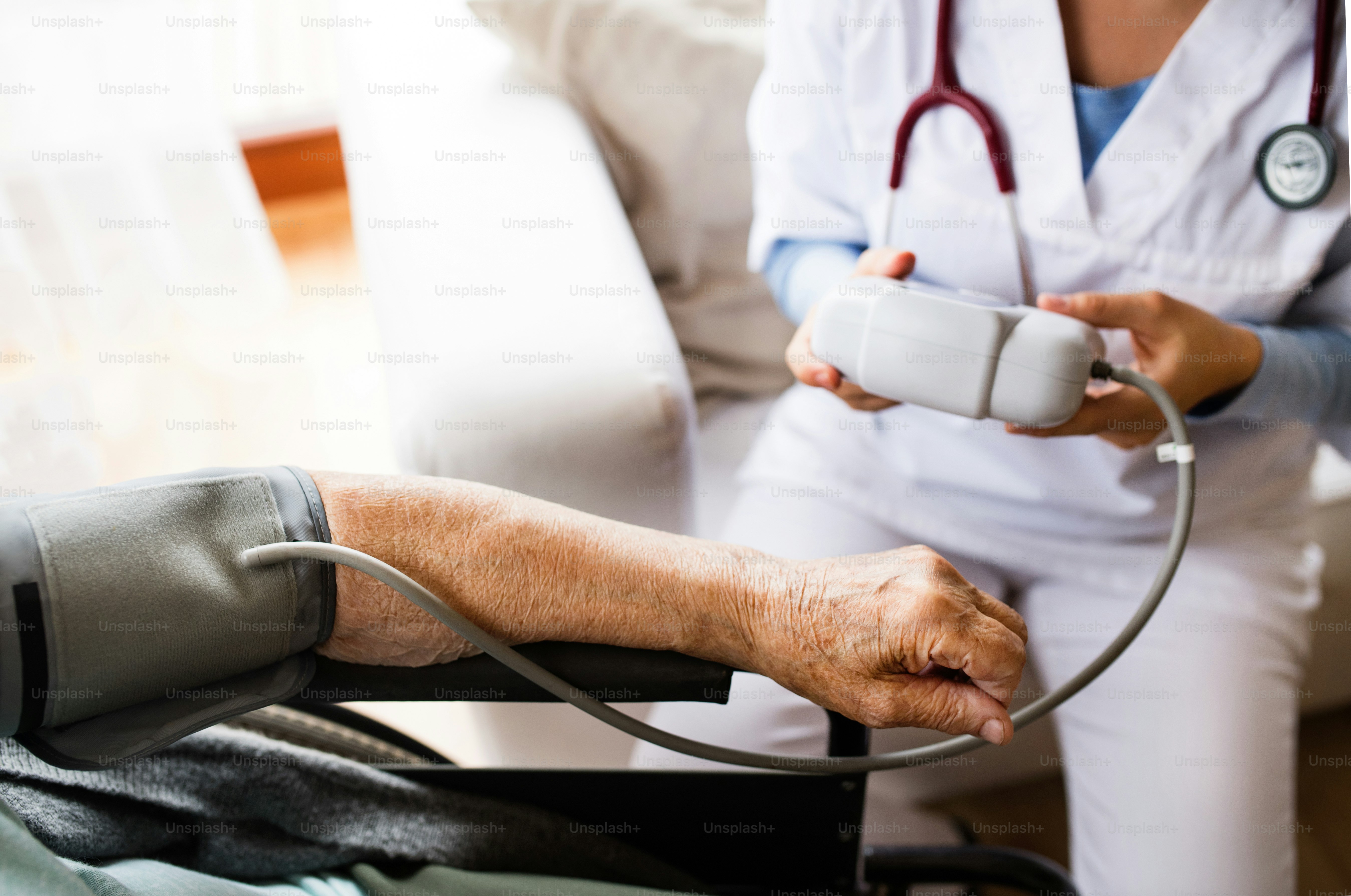 Unrecognizable health visitor and a senior woman during home visit. A nurse checking blood pressure of a woman in an wheelchair