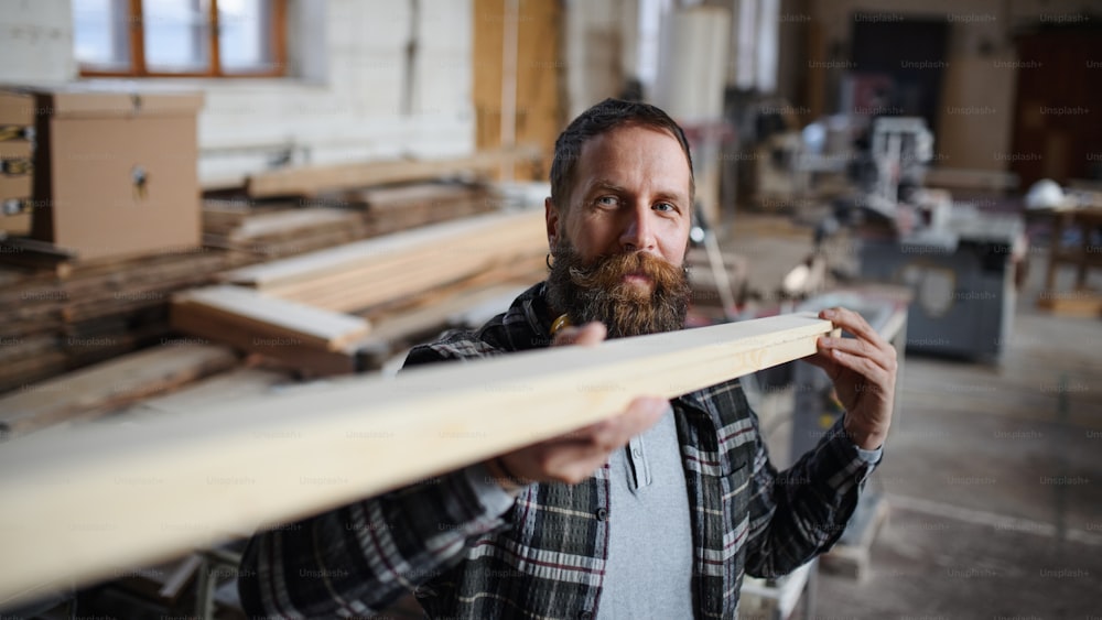 大工工房で木の板を室内に運ぶ成熟した男性大工。スモールビジネスのコンセプト。