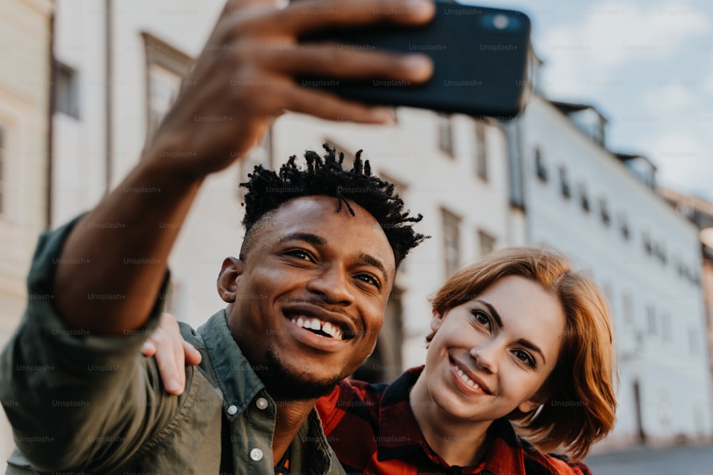 Young biracial couple making selfie for soial networks outdoors in a town.