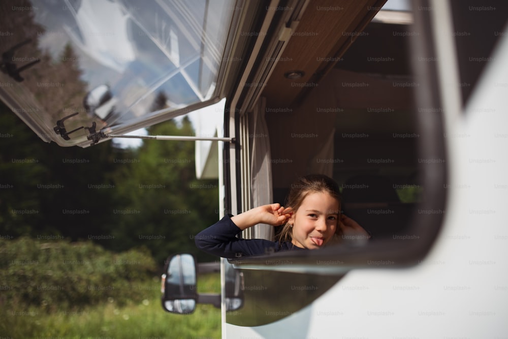 A small girl looking out through caravan window and making faces, family holiday trip.