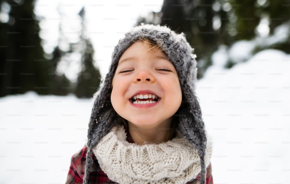 Ritratto ravvicinato di vista frontale di allegra bambina piccola in piedi nella natura invernale, guardando la macchina fotografica.
