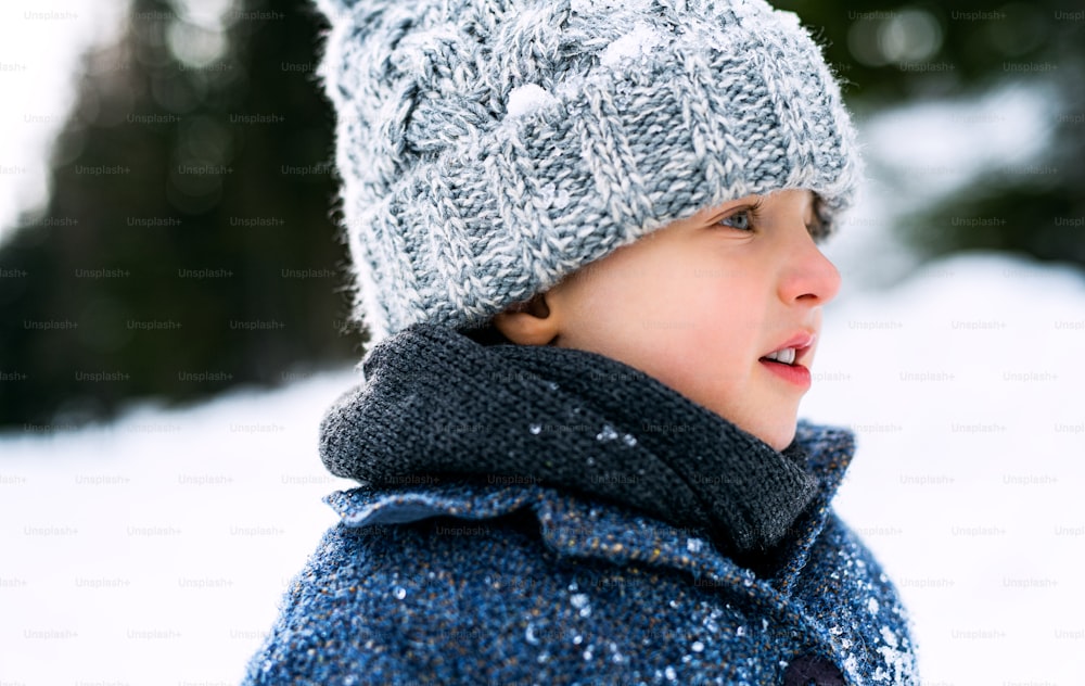Side view of happy small child standing in snow, holiday in winter nature.