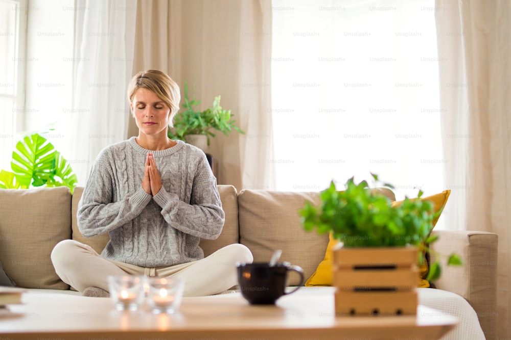 Retrato de mulher dentro de casa fazendo yoga, no sofá, saúde mental e conceito de meditação.