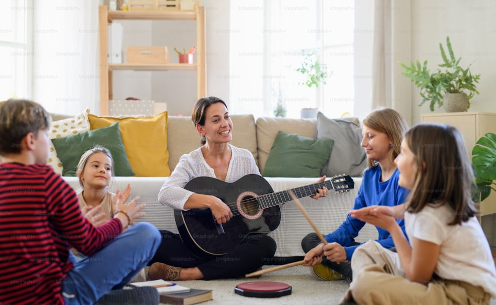 Group of cheerful homeschooling children with teacher having music lesson indoors, coronavirus concept.
