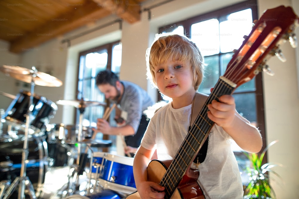 Porträt eines glücklichen kleinen Jungen mit Vater drinnen zu Hause, Schlagzeug und Gitarre spielend.