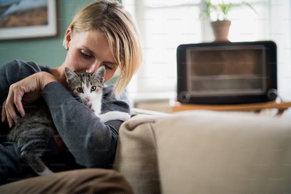 Portrait of happy woman with cat relaxing indoors at home, mental health care concept.