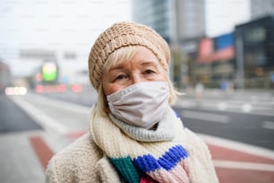 Portrait of happy senior woman standing outdoors on street in city, looking at camera. Coronavirus concept.