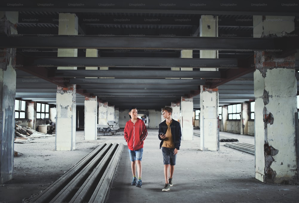 Teenagers boys gang walking indoors in abandoned building, using smartphone.