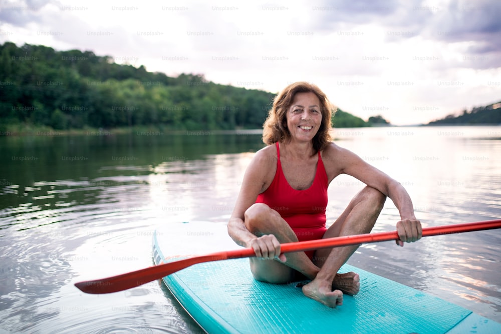 Vista frontale della donna anziana che fa paddleboarding sul lago in estate. Copia spazio.
