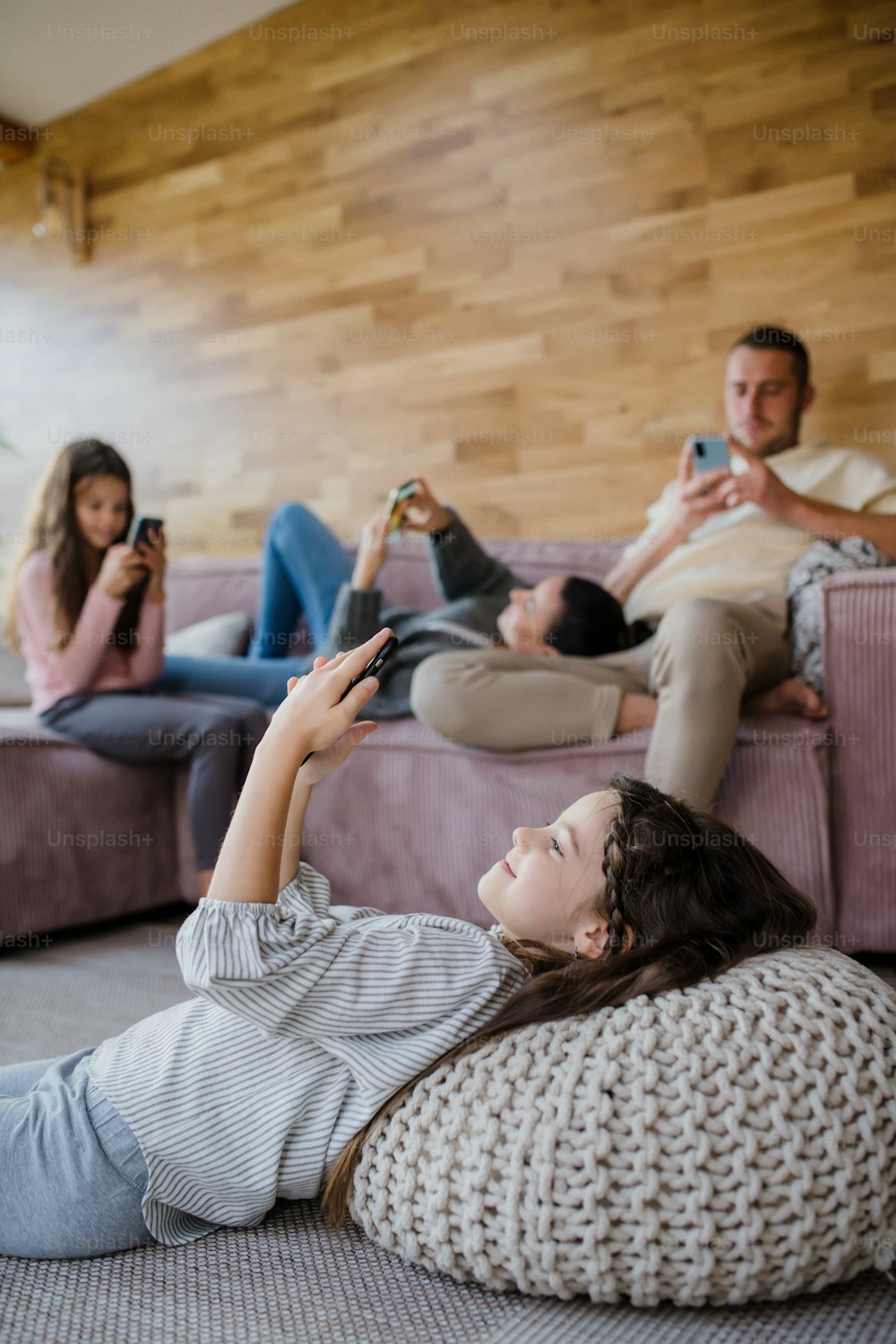 Uma família com duas filhas pequenas, todos estão usando celular na sala de estar.