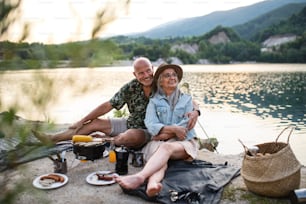 Portrait of happy senior couple resting on summer holiday trip, barbecue by lake.