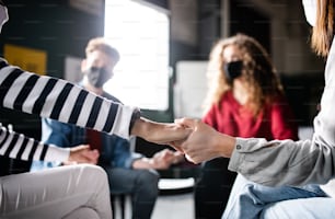 Men and women sitting in a circle during group therapy, holding hands. Coronavirus concept.