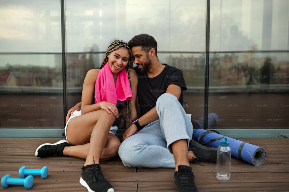 Um jovem casal apaixonado descansando após o exercício ao ar livre no terraço, esporte e conceito de estilo de vida saudável.
