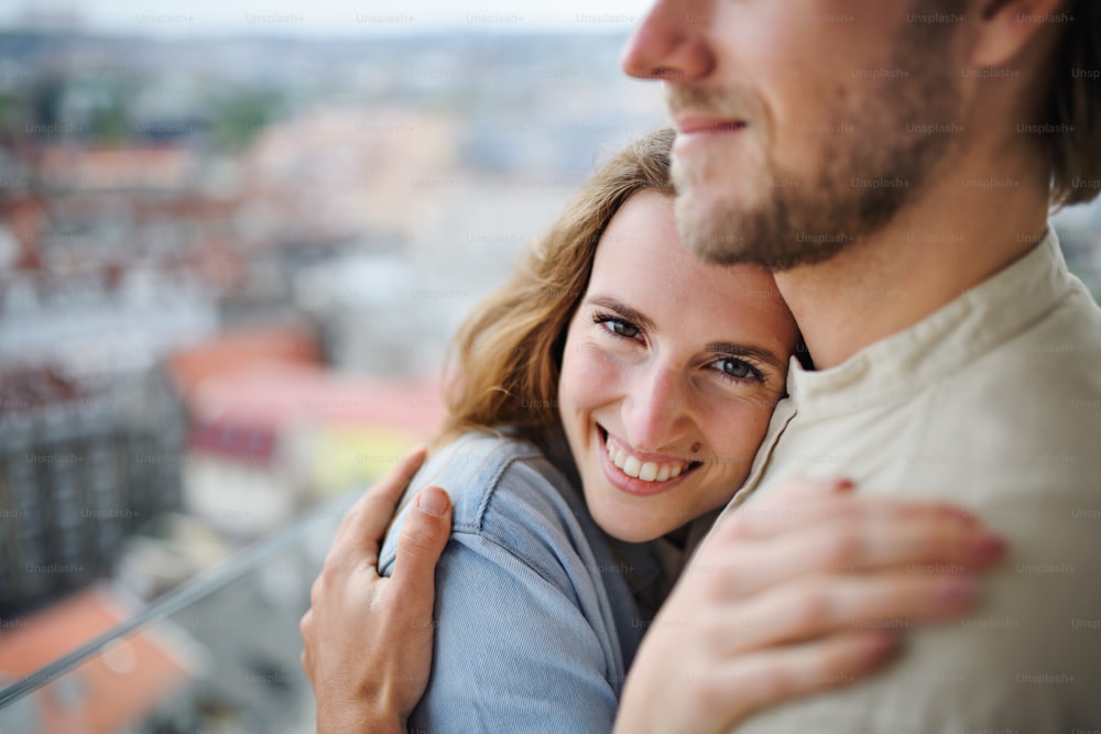 Una feliz pareja joven enamorada de pie al aire libre en el balcón de su casa, abrazándose.