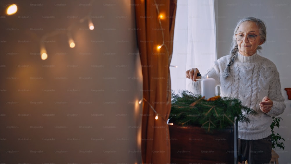 Una mujer mayor enciende una vela en la corona de Navidad en el interior de su casa.
