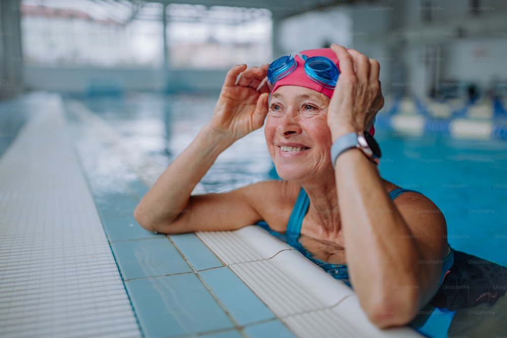 Uma mulher idosa feliz na piscina, apoiada na borda.