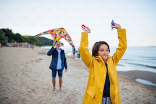 A happy preteen girl and her grandfather playing with kite on sandy beach.