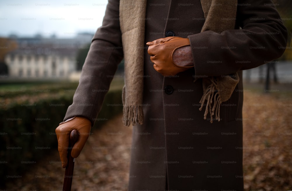 Ein Mittelteil der eleganten älteren Herrenhand mit Gehstock auf Spaziergang im Herbstpark.