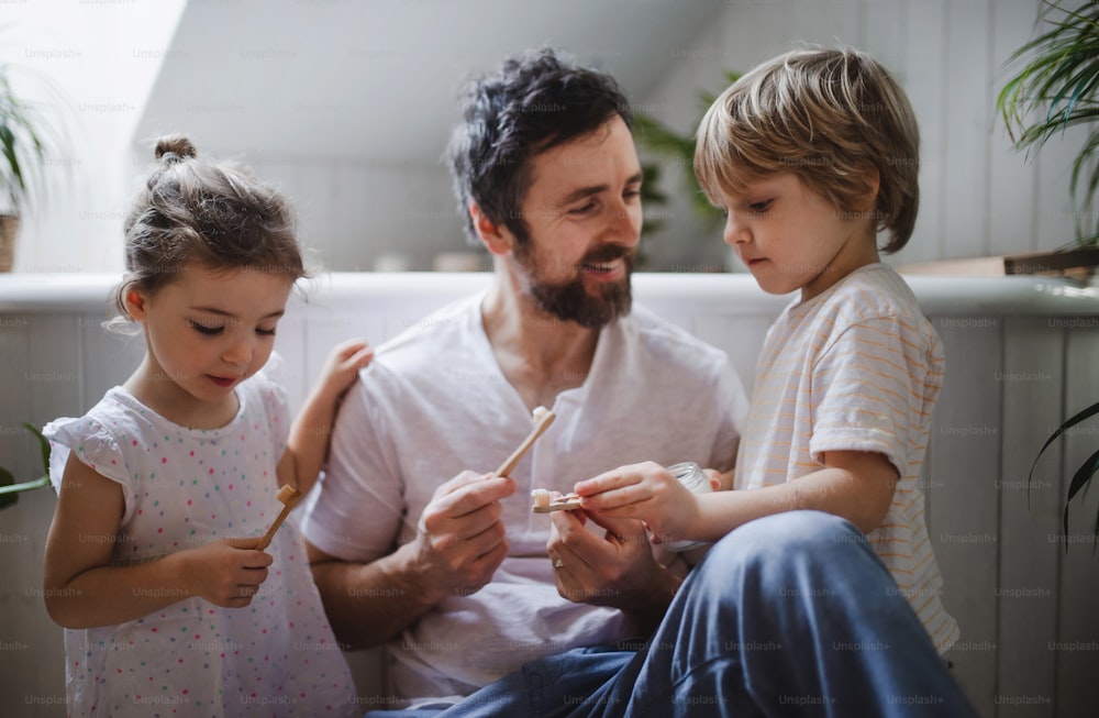 A father with two small children brushing teeth indoors at home, sustainable lifestyle concept.