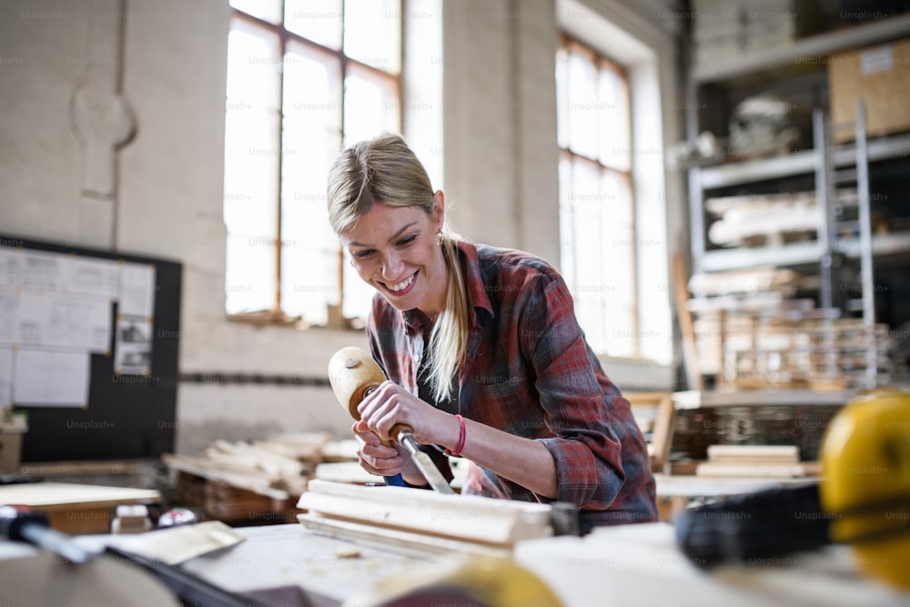 Une menuisière heureuse travaillant sur son produit à l’intérieur dans un atelier de menuiserie.