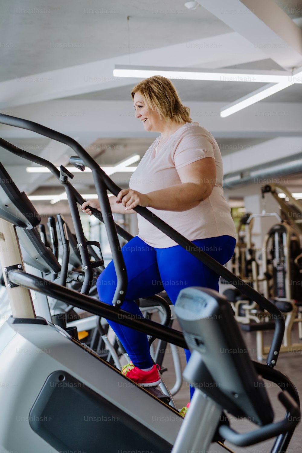 Una mujer adulta mediana feliz con sobrepeso que hace ejercicio en stepper en el interior del gimnasio